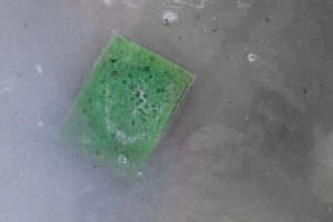 Green dirty sponge floating in dirty grey water