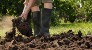 Farmer in black boots digging in soil with shovel