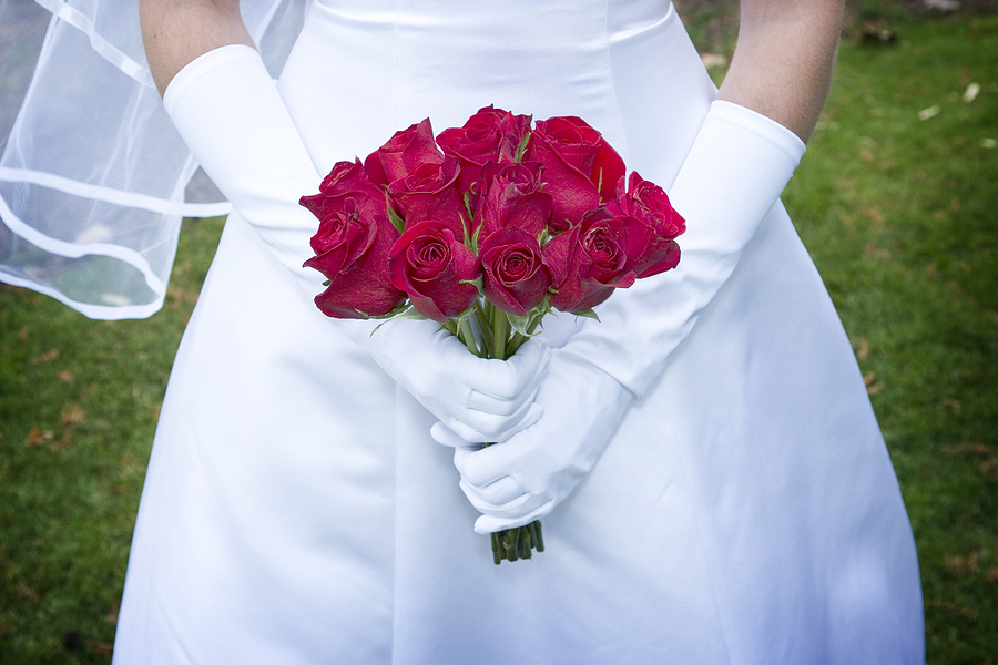 bride in white wedding dress holding red roses